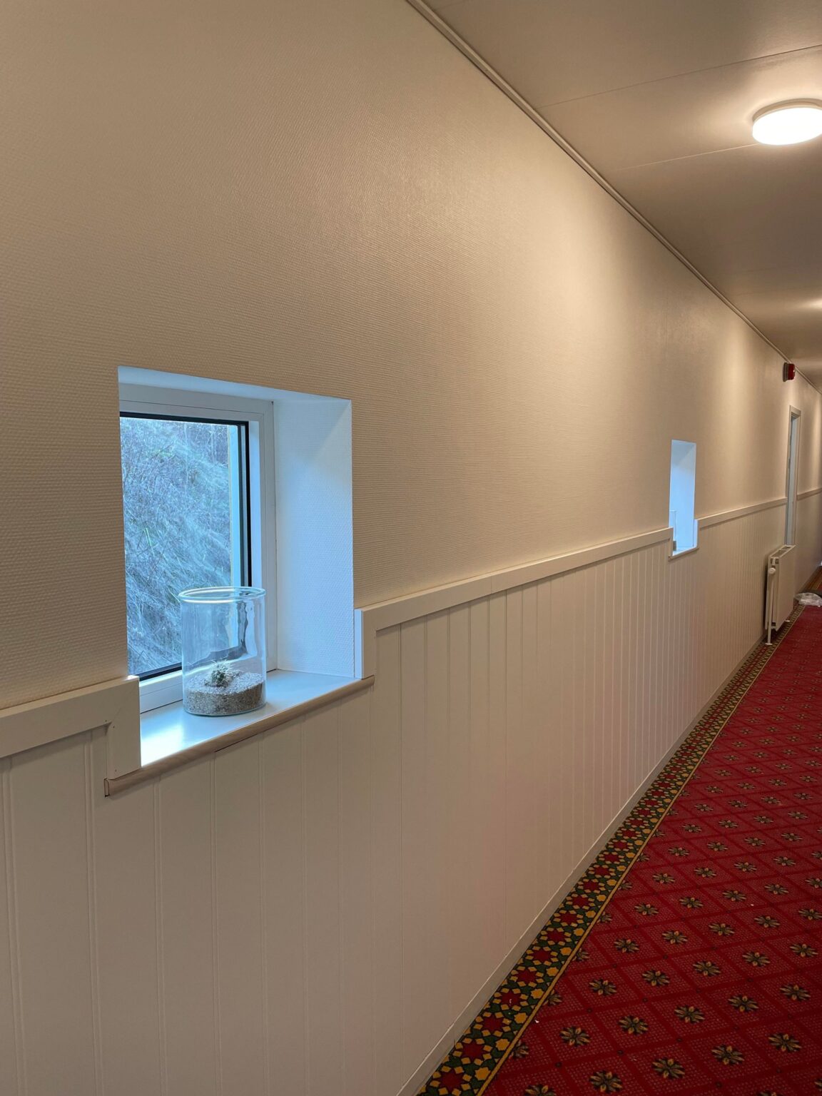 Lys gang med rødt tæppe og små vinduer